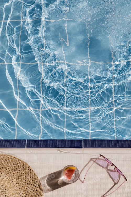 Preview: Straw hat, sunglasses and cocktail on swimming pool side. Blue sea surface with waves, texture water
