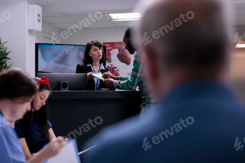 Preview: Healthcare center receptionist holding clipboard for man to sign before doctor appointment