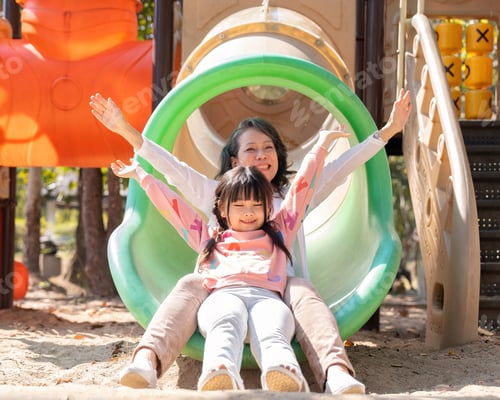 Preview: Happy Asian little girl playing on slider, enjoys playing on playground with her grandmother