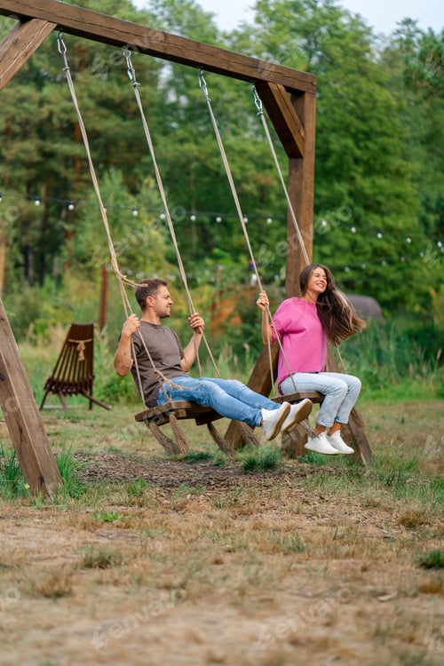 Preview: Loving couple man and girl riding on a large wooden swing overlooking a beautiful lake in nature