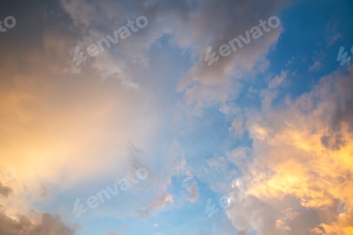 Preview: Dramatic cloudy sunset landscape with puffy clouds lit by orange setting sun and blue sky