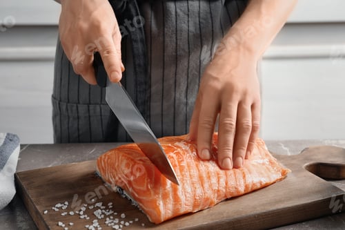 Preview: Woman cutting raw salmon fillet on wooden board