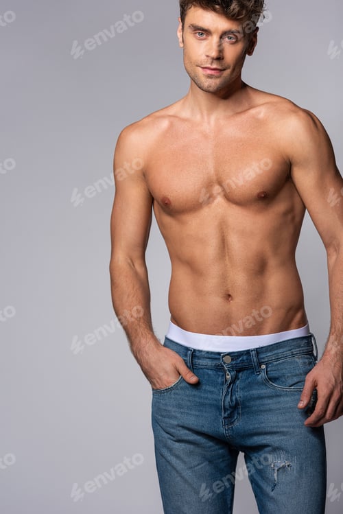 Preview: muscular man in blue jeans standing with hand in pocket isolated on grey
