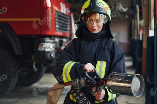 Preview: Hose in hands. Female firefighter in protective uniform standing near truck