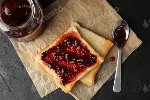 Preview: Toasts and glass jar with jam, spoon and baking paper on black background, top view