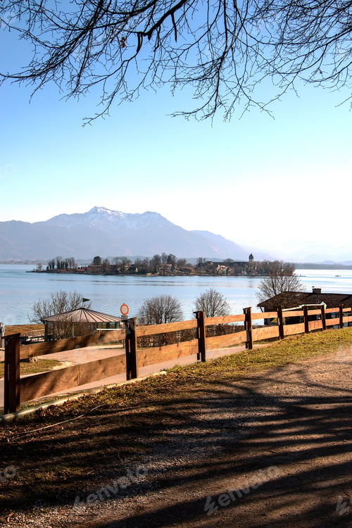 Preview: Vertical shot of a road surrounded by fences with small cottages near a lake surrounded by hills