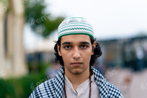 Preview: portrait of a young Arab man who prays and looks at camera against the backdrop of a Muslim mosque