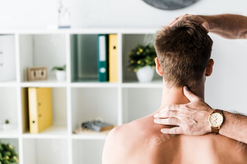 Preview: cropped view of doctor touching neck of shirtless patient sitting in clinic