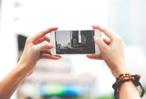 Preview: Hands holding mobile phone screen showing metro landscape city view photo
