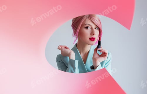 Preview: Young girl with pink hair and in blue jacket holding lipstick.
