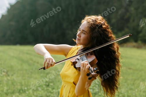 Preview: A young attractive curly-haired brunette walks in the field with violin
