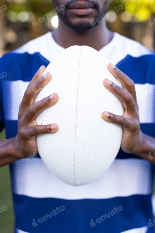 Preview: African American young male athlete on field outdoors holding a rugby ball, wearing a striped shirt