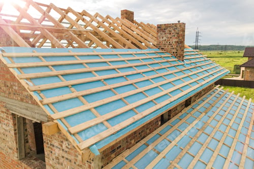 Preview: Aerial view of a brick house with wooden roof frame under construction.