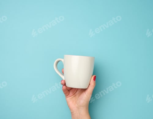 Preview: Female hand holds a ceramic mug on a blue background, break time and drink coffee