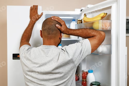 Preview: African american man standing in front of open fridge and choosing food