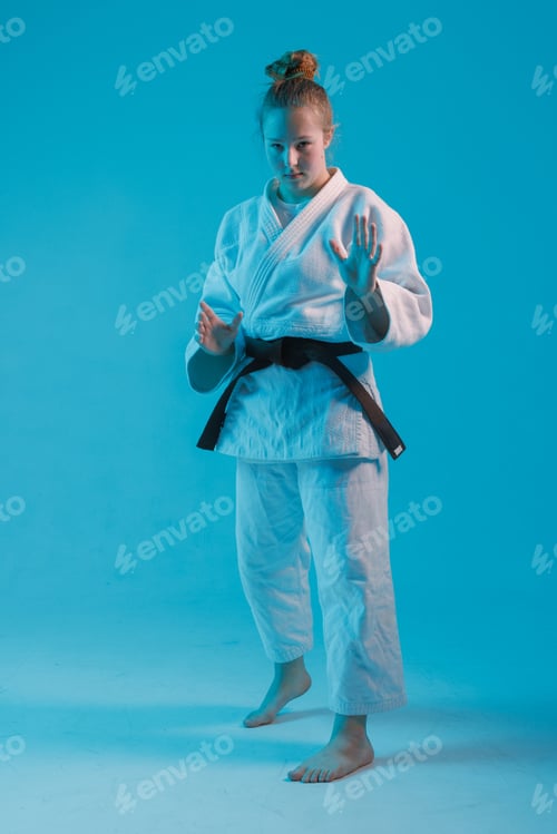 Preview: girl judoka in a white kimano with a black belt on a blue background, studio photo