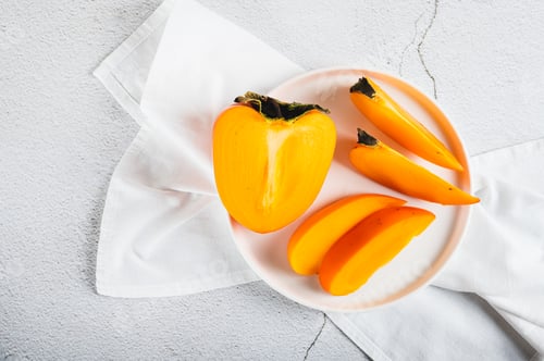 Preview: Closeup of sliced ripe fresh persimmon on a plate on the table top view
