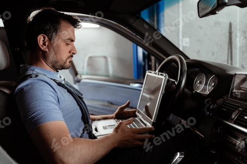Preview: Car mechanic works on a laptop inside a vehicle at an auto shop during the day