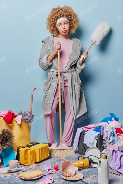 Preview: Full length shot of thoughtful displeased housewife sweeps floor and dusts furniture poses at messy