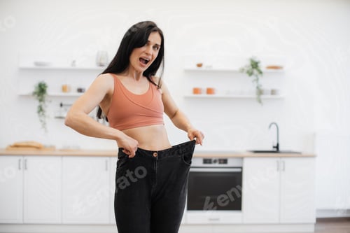 Preview: Woman looking at oversized jeans on thin waist at home