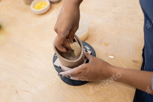 Preview: Cropped view of african american craftswoman forming clay product with sponge