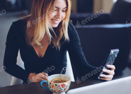 Preview: Young teenage girl sitting at a table drinking tea smiling and taking a selfie with mobile phone
