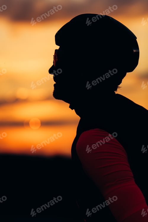 Preview: Side view of road cyclist in helmet posing during sunset