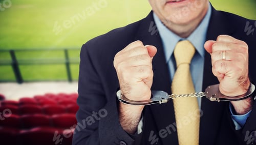 Preview: Closeup Of Businessman With Handcuffed Hands Against Red Bleachers Looking Down On Football Pitch