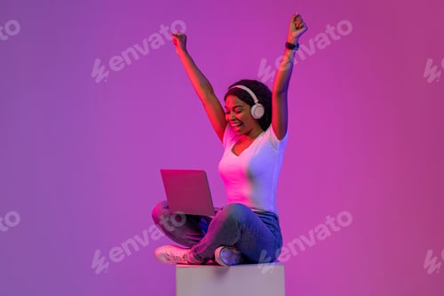 Preview: Online Win. Happy Black Woman Celebrating Success With Laptop In Neon Light