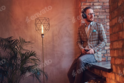 Preview: Stylish man in a flannel suit and glasses listening music in a room with loft interior.