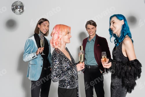 Preview: happy nonbinary friends with champagne glasses smiling at each other near queer people on grey
