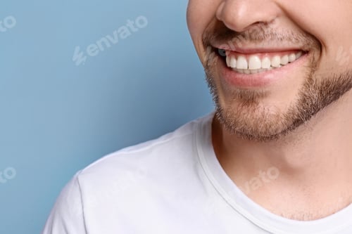 Preview: Young man with beautiful smile on grey background. Teeth whitening