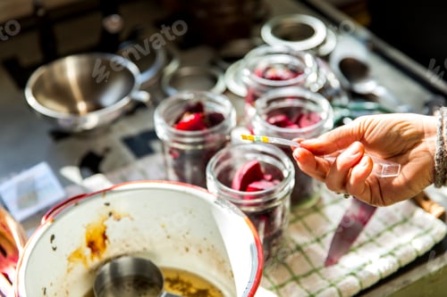Preview: Hand of woman PH testing beetroot preserves jars in kitchen