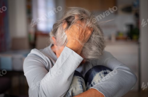 Preview: Frustrated depressed old woman covering face with hand in the hairs, sitting on couch at home alone
