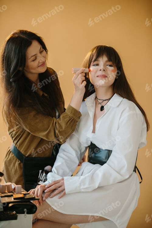 Preview: Behind-the-Scenes: Makeup Artist Prepares Model for Photoshoot in Studio with Beige Background