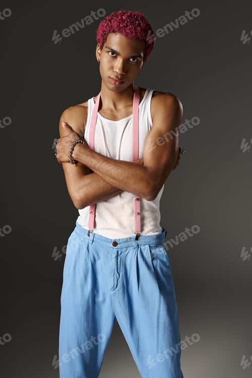 Preview: handsome man in blue pants with pink suspenders posing with slightly crossed arms, fashion concept