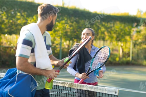 Preview: Happy caucasian couple playing tennis talking over the net on sunny outdoor tennis court