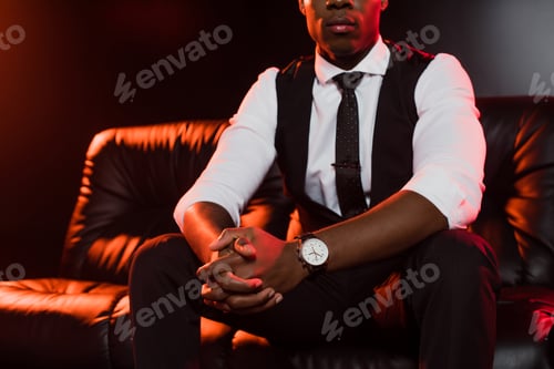 Preview: cropped view of african american man in suit sitting on sofa with clenched hands on black background