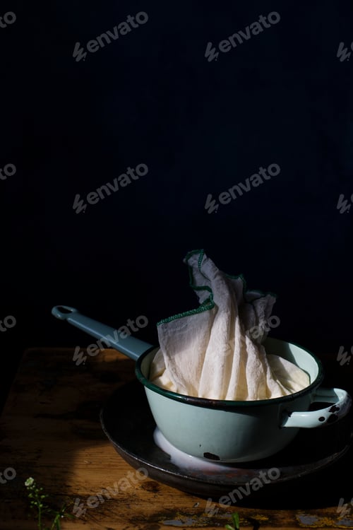 Preview: Pot with prepared to press cottage cheese on a table.