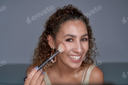 Preview: Cheerful woman shading glowing highlighter powder with brush on