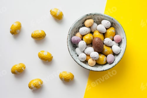 Preview: Easter chocolate eggs candy in a round bowl on yellow and white background, sweet food flat lay