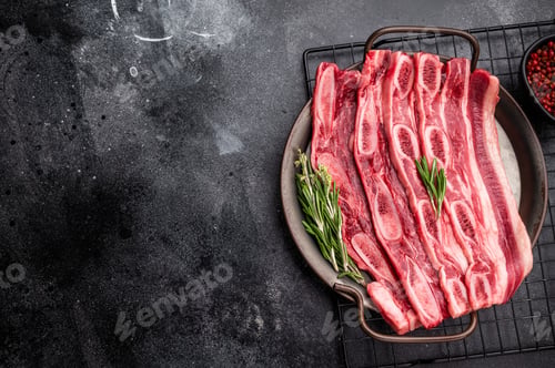 Preview: Raw Flanken cut beef short ribs (Kalbi) with rosemary and thyme on a dark