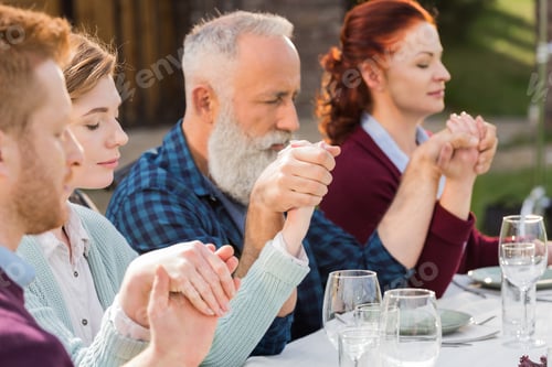 Preview: family holding hands while praying during dinner at countryside