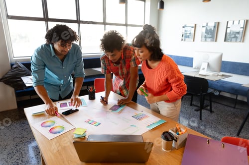 Preview: Creative multiracial design professionals discussing over charts at table in office