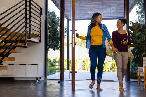 Aperçu: Happy biracial lesbian couple coming home from shopping, copy space