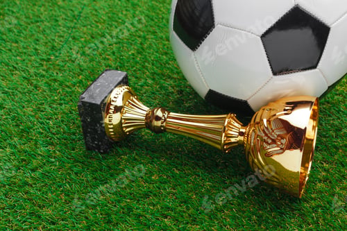 Preview: Golden trophy and soccer ball on green grass after a competitive match
