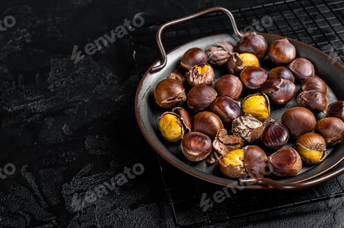 Preview: Cracked roast chestnuts served in a tray. Black background. Top view. Copy space