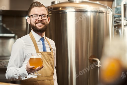 Preview: Bearded brewer holding cold beer glass with foam