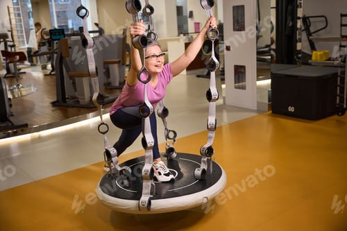Preview: Middle aged european woman wearing sportswear doing exercise on hanging mat