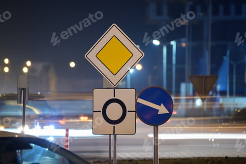 Preview: Roundabout road signs with blurred cars on city street traffic at night.